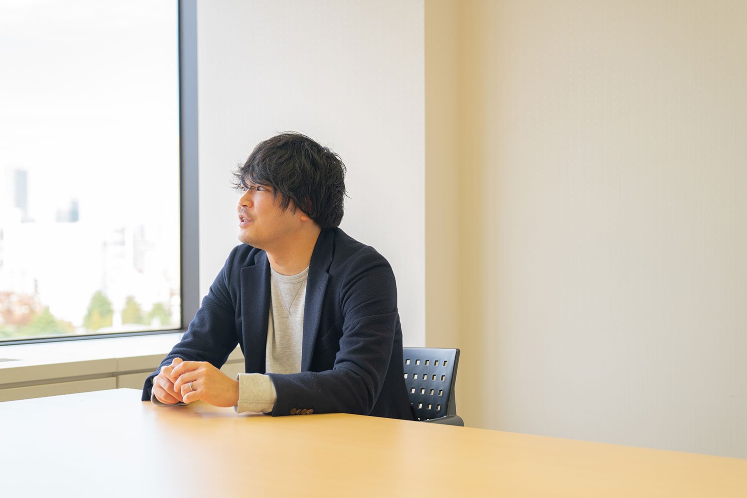 会議室で窓の外に視線を送りつつ、過去の出来事を思い出す佐賀文昭さん